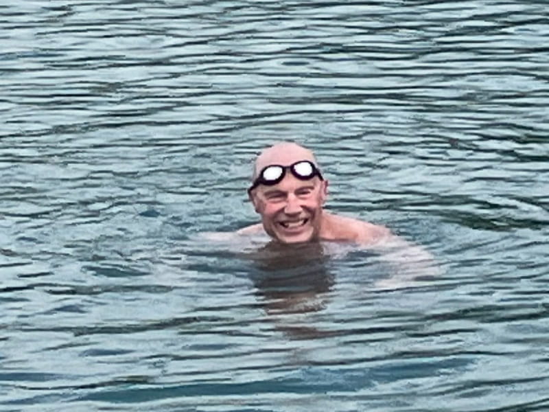 Don Milich smiling and swimming in a body of water with goggles pulled up on his forehead