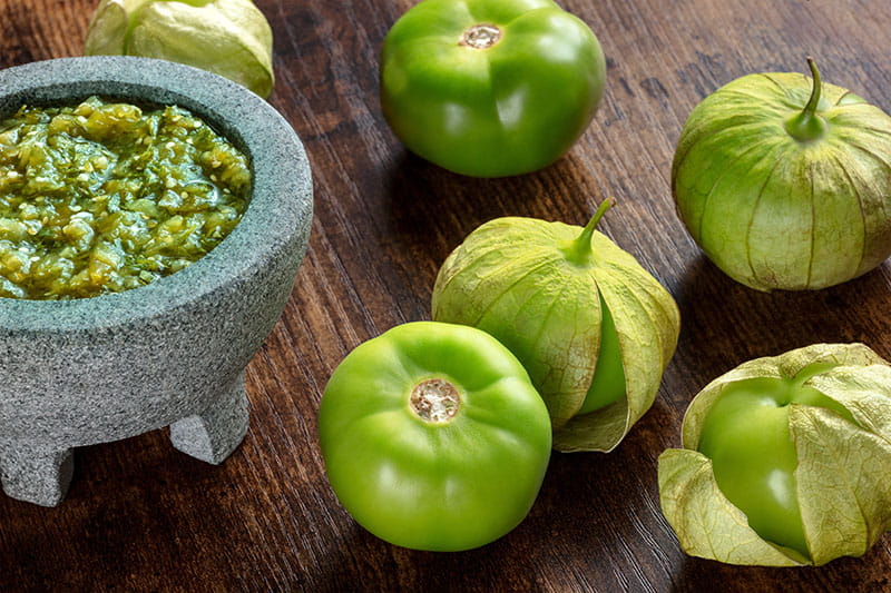 close-up of fresh tomatillos on a table next to a dish of tomatillo salsa