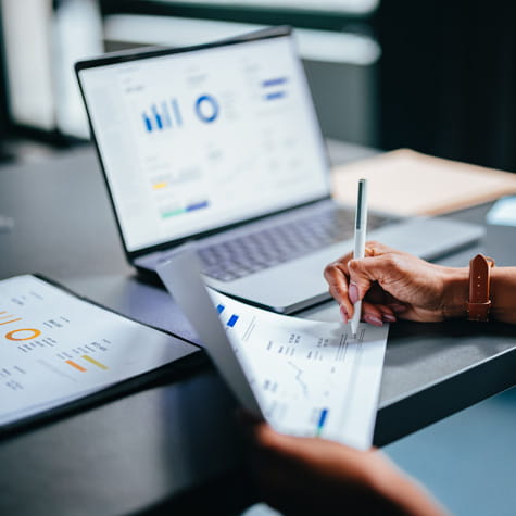 close up of hands holding a chart in front of a laptop showing data