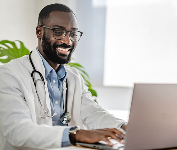 stock photo of young male doctor typing on a laptop